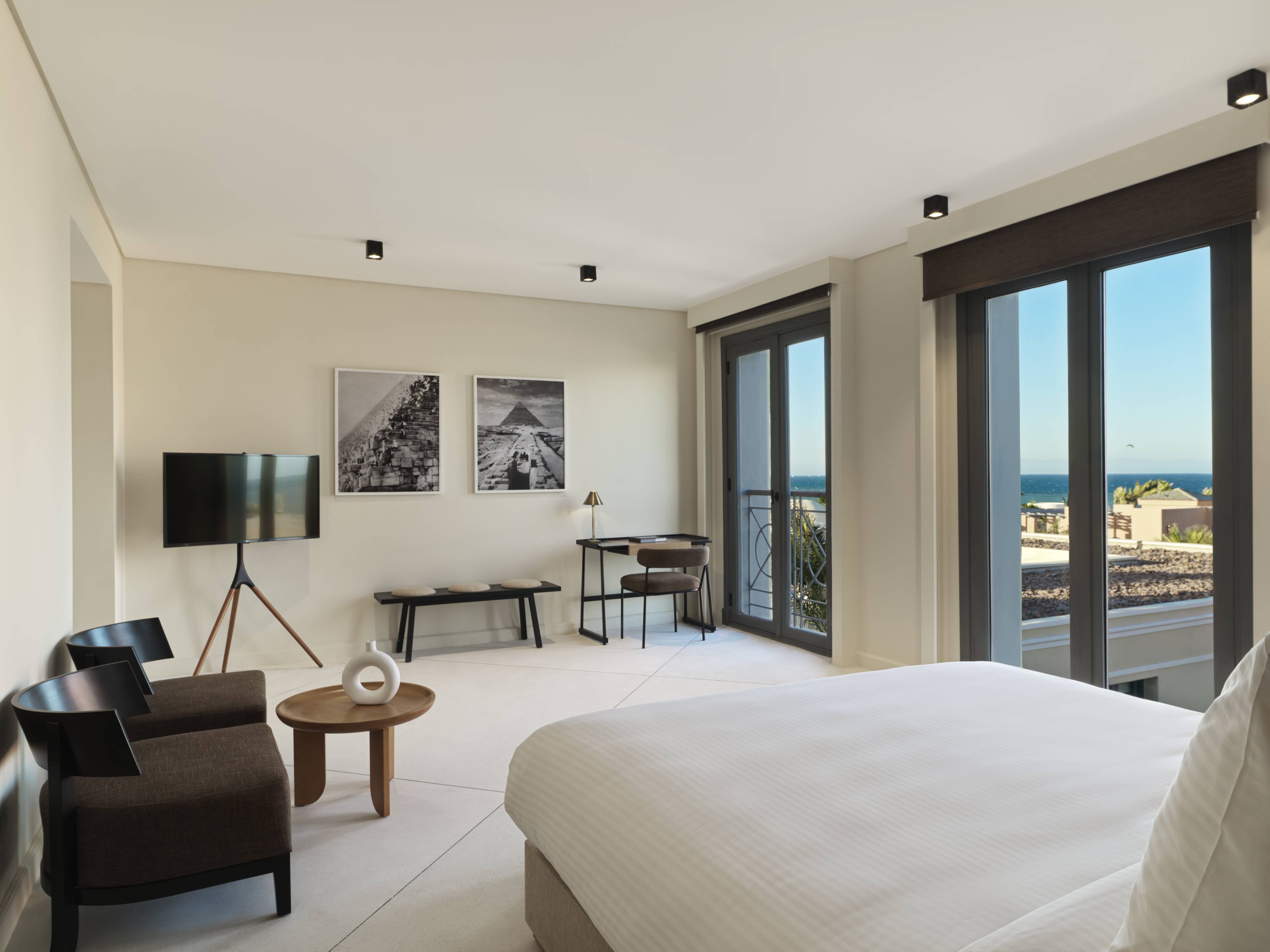 Bedroom with many facilities, king bed, TV, Chairs, and big windows overlooking the sea at The Chedi El Gouna Hotel